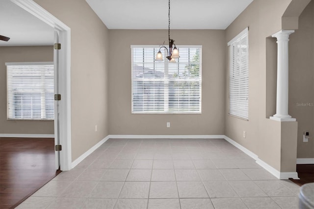 unfurnished dining area featuring light tile patterned flooring, a chandelier, and ornate columns