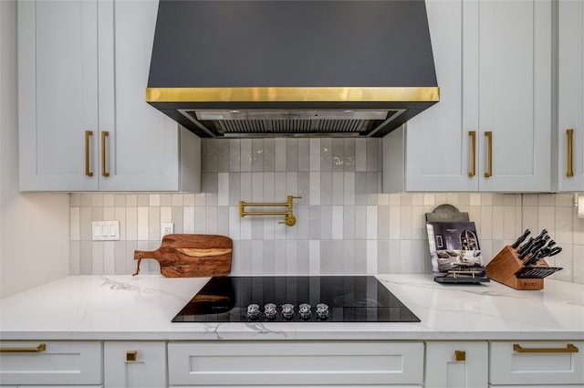 kitchen featuring black electric cooktop, island range hood, tasteful backsplash, and light stone countertops