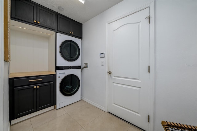 laundry area with cabinets, stacked washer and clothes dryer, light tile patterned floors, and a textured ceiling