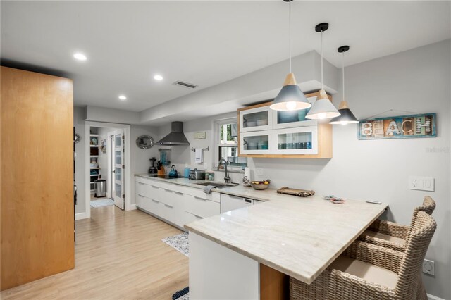 kitchen featuring decorative light fixtures, a kitchen breakfast bar, kitchen peninsula, and wall chimney exhaust hood