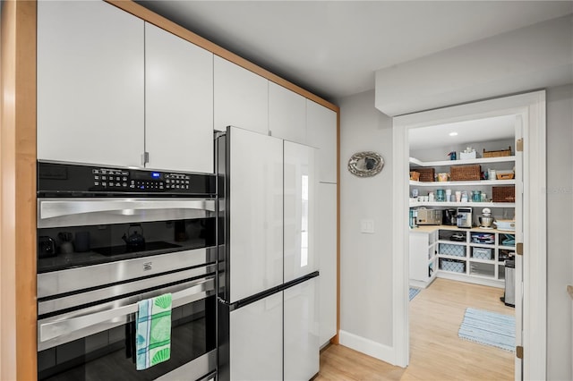 kitchen featuring white cabinetry, double oven, light wood-type flooring, and refrigerator