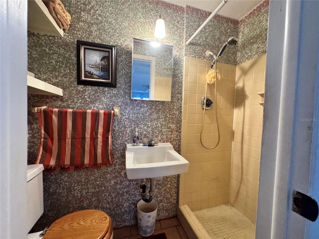 bathroom featuring a tile shower, sink, tile patterned flooring, and toilet