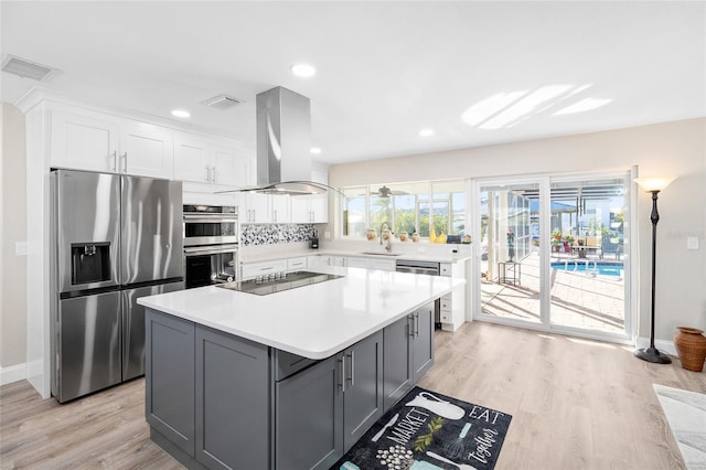 kitchen with appliances with stainless steel finishes, island range hood, white cabinetry, sink, and a center island