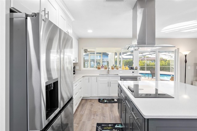 kitchen with white cabinetry, sink, island exhaust hood, stainless steel appliances, and light wood-type flooring