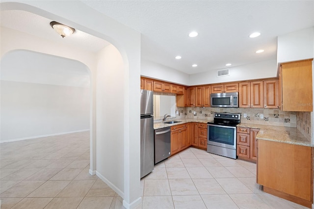 kitchen featuring sink, light tile patterned floors, stainless steel appliances, tasteful backsplash, and light stone countertops