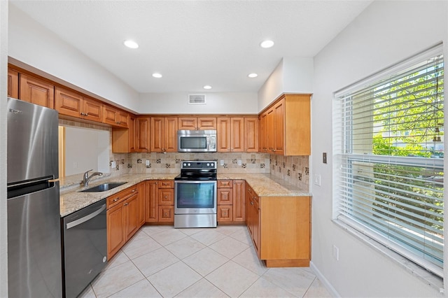 kitchen featuring stainless steel appliances, light stone countertops, sink, and backsplash