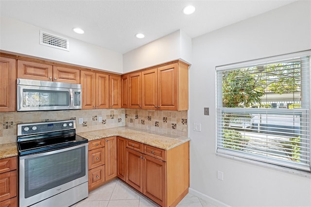 kitchen with tasteful backsplash, light stone countertops, appliances with stainless steel finishes, and light tile patterned flooring