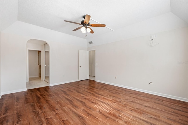 empty room with lofted ceiling, hardwood / wood-style floors, a raised ceiling, and ceiling fan