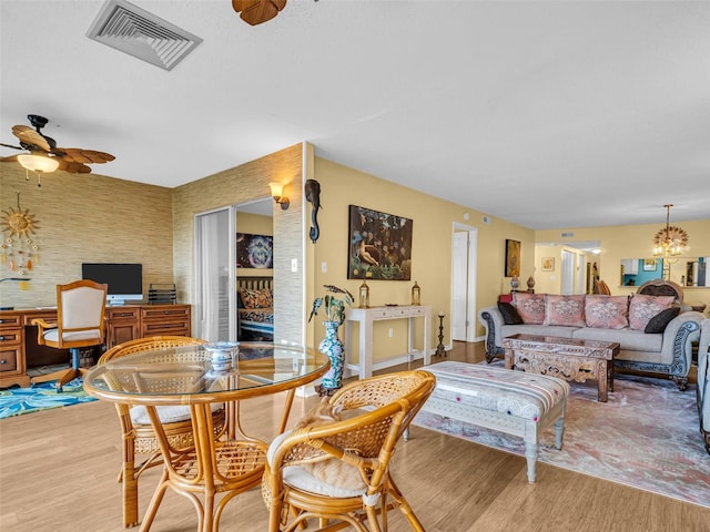 dining area featuring light wood-type flooring, visible vents, built in study area, and ceiling fan with notable chandelier