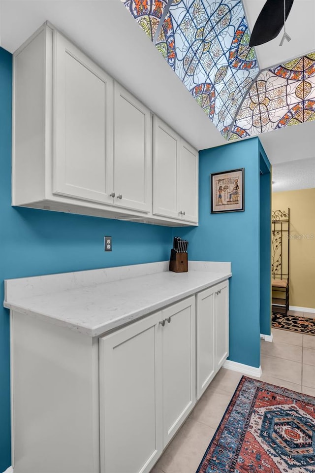 kitchen featuring light tile patterned floors, light stone counters, white cabinetry, and baseboards