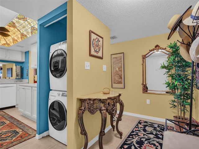 laundry area featuring a textured ceiling, light tile patterned flooring, laundry area, stacked washer and dryer, and visible vents