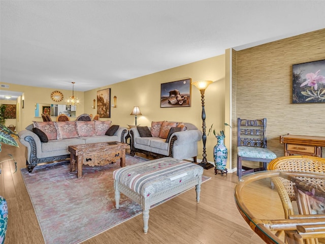 living room with light wood-style floors, an accent wall, visible vents, and an inviting chandelier