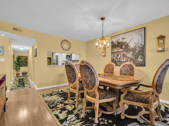 dining room with baseboards, light wood finished floors, visible vents, and a notable chandelier