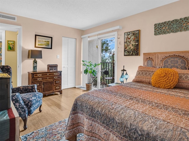 bedroom with access to exterior, light wood-style flooring, visible vents, and a textured ceiling