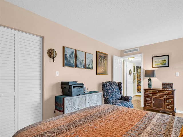 bedroom with baseboards, visible vents, wood finished floors, a textured ceiling, and a closet