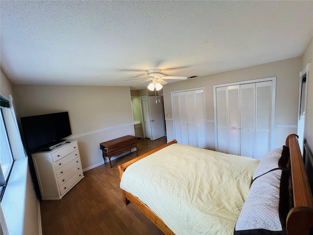 bedroom featuring dark hardwood / wood-style floors, two closets, a textured ceiling, and ceiling fan