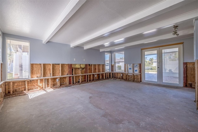 unfurnished room with a healthy amount of sunlight, wooden walls, concrete floors, and beamed ceiling