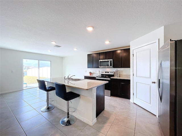 kitchen with light tile patterned flooring, sink, a breakfast bar area, an island with sink, and stainless steel appliances