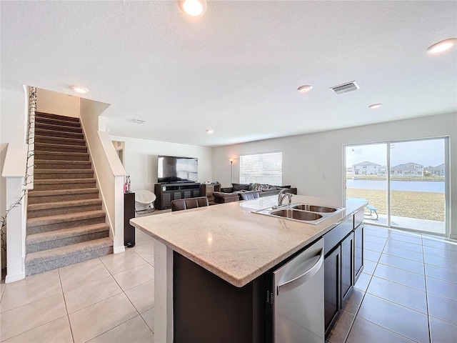 kitchen with sink, light tile patterned flooring, stainless steel dishwasher, and a center island with sink