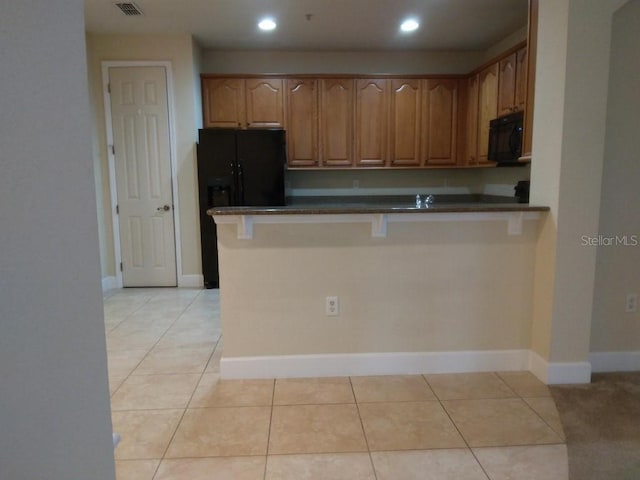 kitchen featuring black appliances, light tile patterned floors, a kitchen breakfast bar, and kitchen peninsula