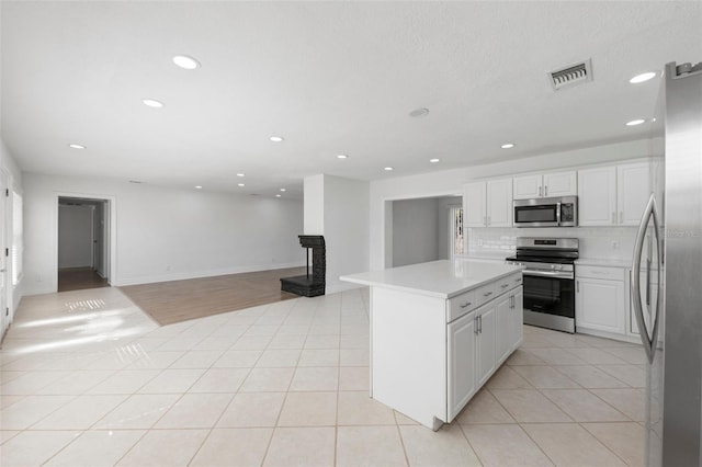 kitchen with light tile patterned flooring, white cabinetry, a kitchen island, stainless steel appliances, and backsplash