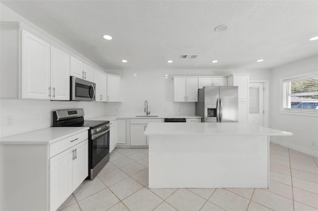 kitchen with a kitchen island, appliances with stainless steel finishes, white cabinetry, sink, and light tile patterned floors