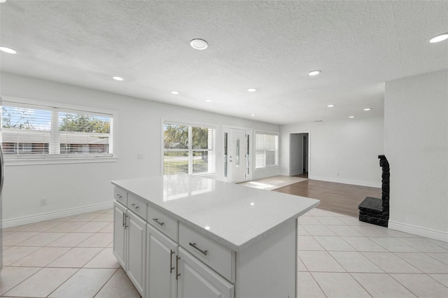 kitchen with white cabinetry, a kitchen island, light tile patterned flooring, and a textured ceiling