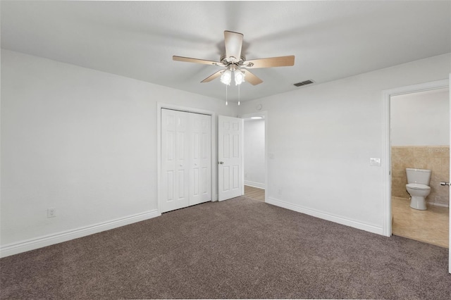 unfurnished bedroom featuring dark carpet, connected bathroom, ceiling fan, and a closet