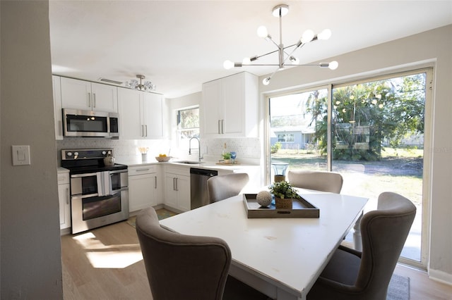 kitchen with appliances with stainless steel finishes, pendant lighting, white cabinets, and light hardwood / wood-style flooring