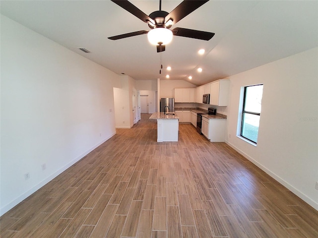 kitchen featuring lofted ceiling, a kitchen island with sink, stainless steel appliances, light hardwood / wood-style floors, and white cabinets