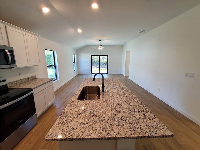 kitchen featuring appliances with stainless steel finishes, open floor plan, a kitchen island with sink, a sink, and white cabinets