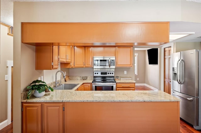 kitchen featuring sink, light stone counters, kitchen peninsula, stainless steel appliances, and light wood-type flooring