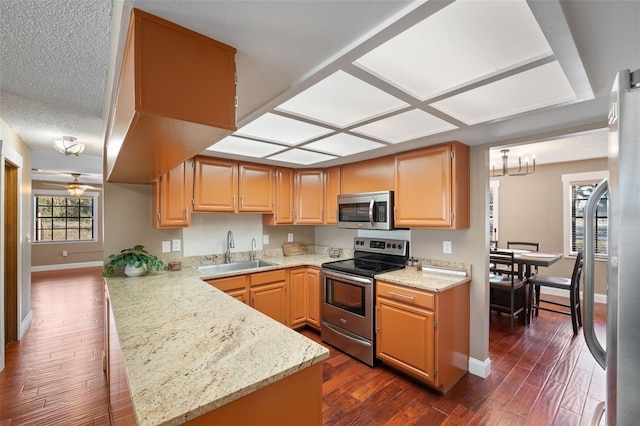 kitchen with sink, dark wood-type flooring, appliances with stainless steel finishes, light stone countertops, and kitchen peninsula