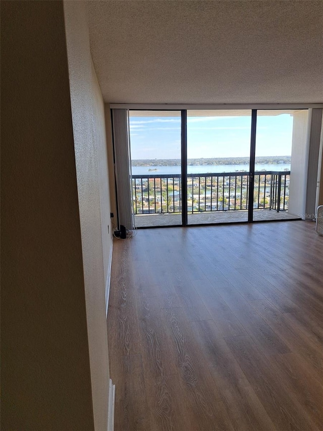 unfurnished room with expansive windows, a water view, dark wood-type flooring, and a textured ceiling