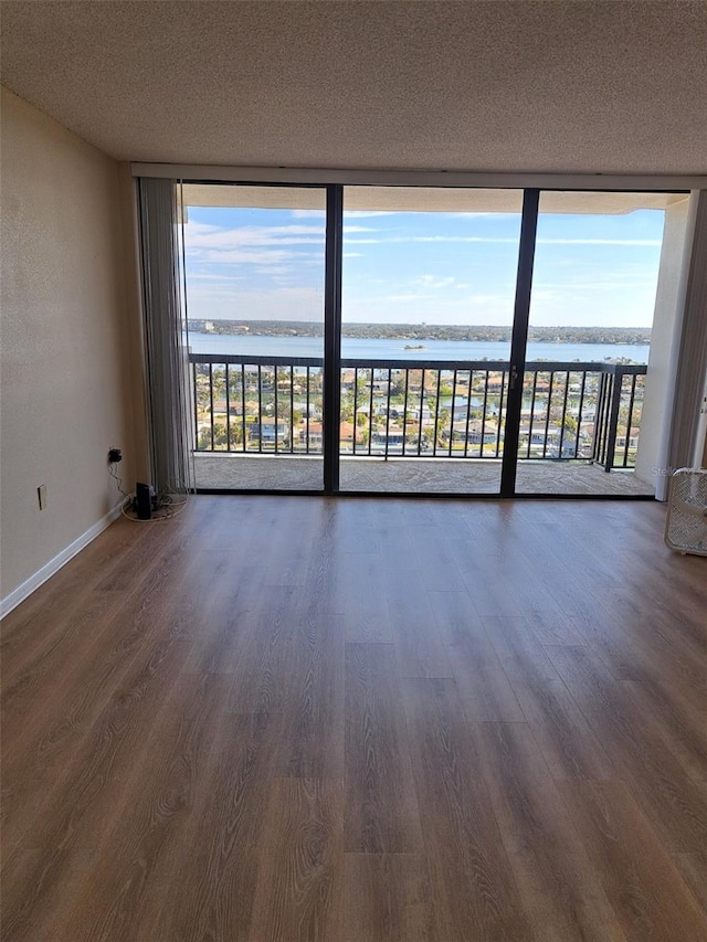 empty room featuring a water view, expansive windows, dark hardwood / wood-style floors, and a textured ceiling