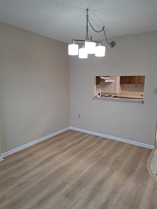 unfurnished dining area featuring a notable chandelier, a textured ceiling, and light wood-type flooring