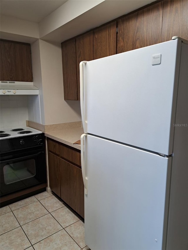 kitchen featuring white fridge, black electric range oven, and light tile patterned floors