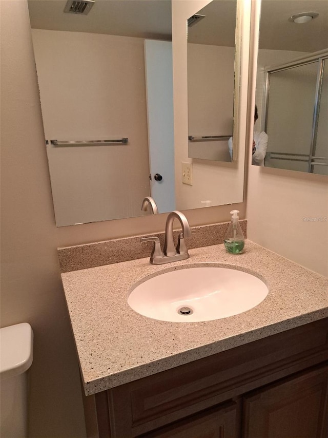 bathroom featuring vanity, walk in shower, and toilet