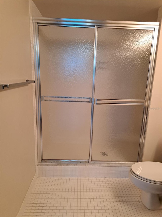 bathroom featuring tile patterned flooring, a shower with shower door, and toilet