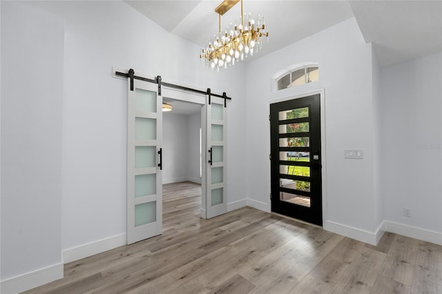 entryway featuring a towering ceiling, a barn door, a chandelier, and light wood-type flooring