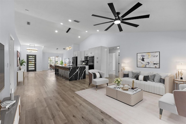 living room featuring sink, ceiling fan with notable chandelier, light hardwood / wood-style flooring, and high vaulted ceiling