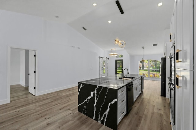 kitchen with white cabinetry, sink, a kitchen island with sink, black appliances, and a barn door