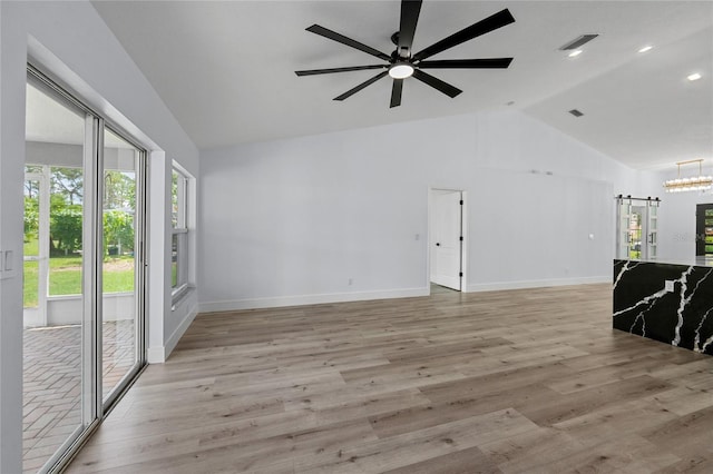 unfurnished living room featuring vaulted ceiling, a barn door, ceiling fan with notable chandelier, and light hardwood / wood-style flooring