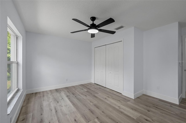 unfurnished bedroom featuring light wood-type flooring, a textured ceiling, ceiling fan, and a closet