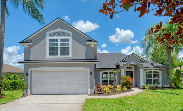 traditional home featuring roof with shingles, driveway, an attached garage, stucco siding, and a front lawn