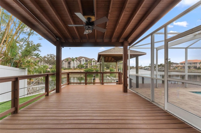 wooden terrace featuring a water view, ceiling fan, and glass enclosure