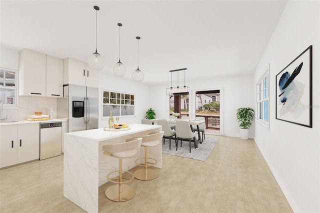 kitchen featuring pendant lighting, stainless steel fridge, dishwashing machine, and white cabinets