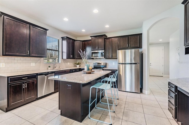 kitchen featuring appliances with stainless steel finishes, sink, a center island, light stone counters, and dark brown cabinetry