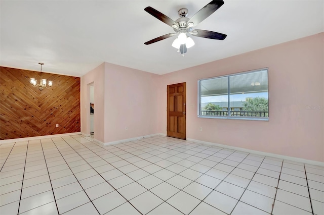 tiled empty room featuring ceiling fan with notable chandelier and wood walls