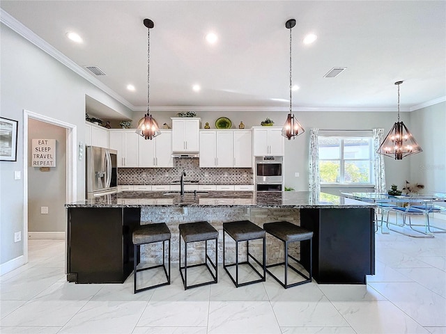 kitchen with appliances with stainless steel finishes, white cabinets, dark stone counters, hanging light fixtures, and a large island